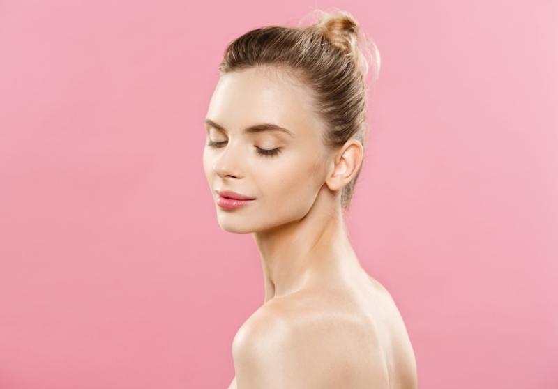 woman with closed eyes and her hair in a bun has closed eyes and standing in front of a pink background