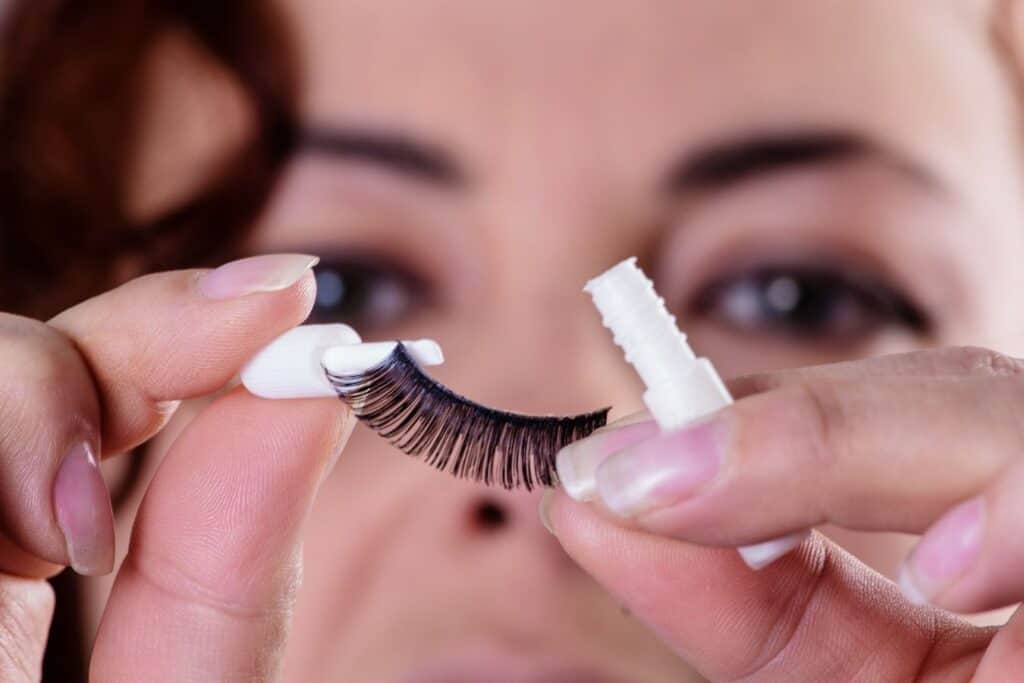 woman holding up a fake lash and applying eyelash glue