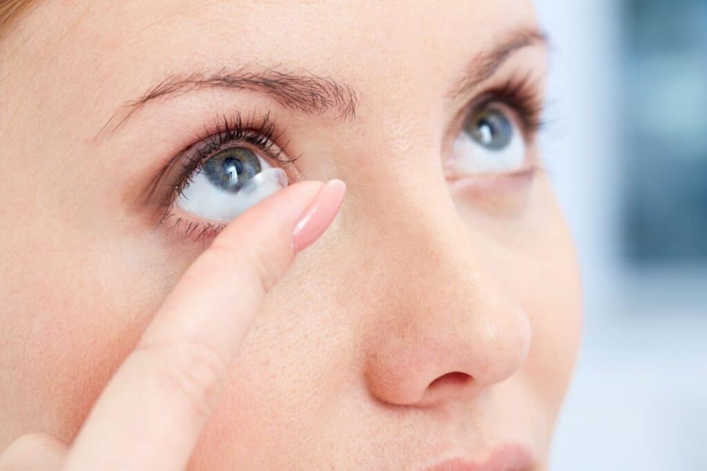 woman looking up, finger close to her with a contact lens, she is about to put it into her eye.