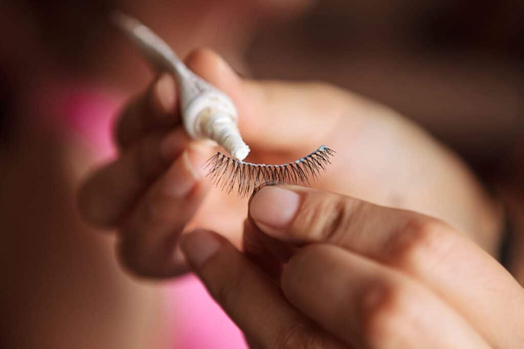 Woman applying eyelash glue to a fake eyelash.