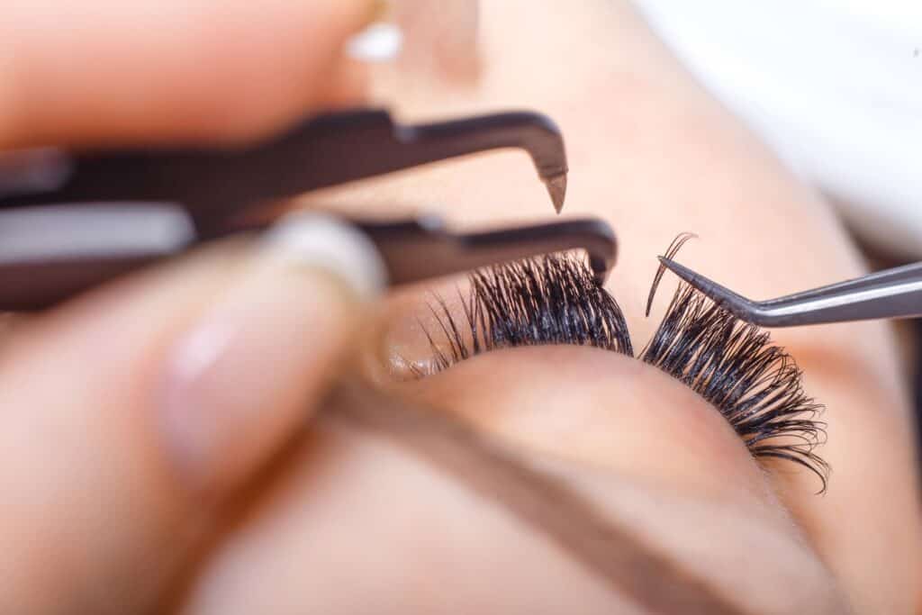 woman adding eyelash extensions to a client