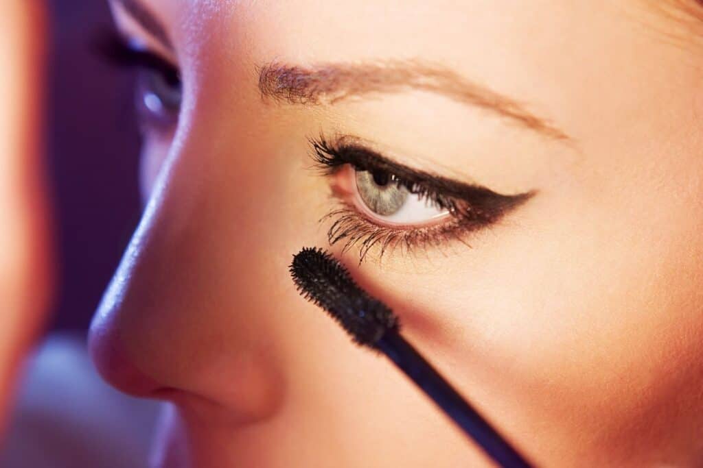 woman applying mascara to her bottom lashes in dim lighting