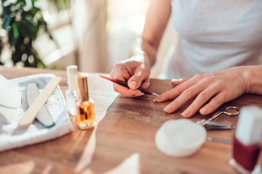woman doing a manicure on her own nails on a brown table with nail polishes and files around her
