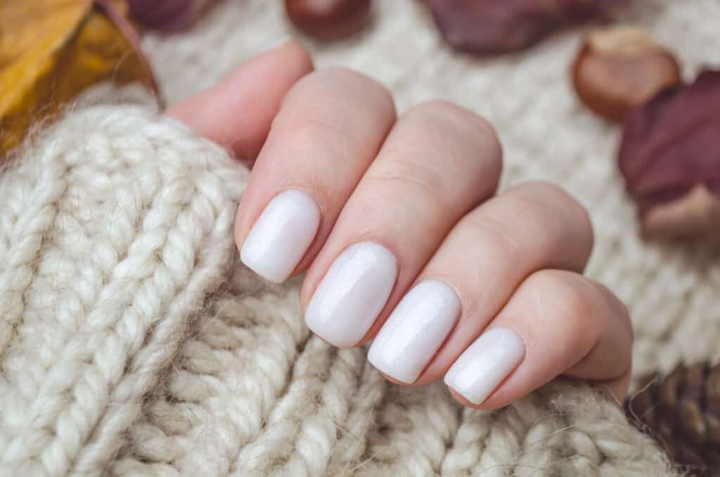 a hand with white fingernails and a white wholly jumper