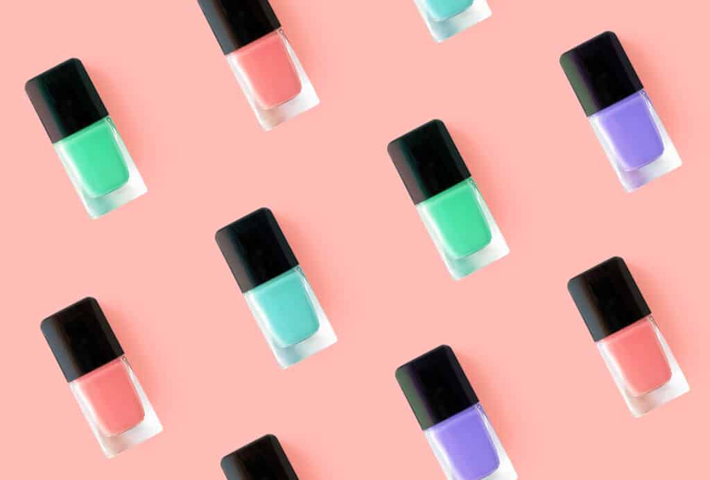 a variety of nail polish bottles lying in front of a pink background.