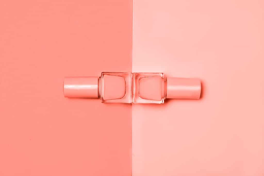 a close up of two nail polish bottles lying in front of a peach background.