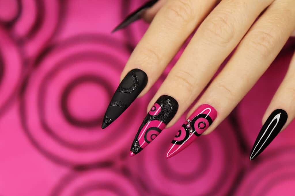 four fingers with very long black and pink nails in front of a pink background