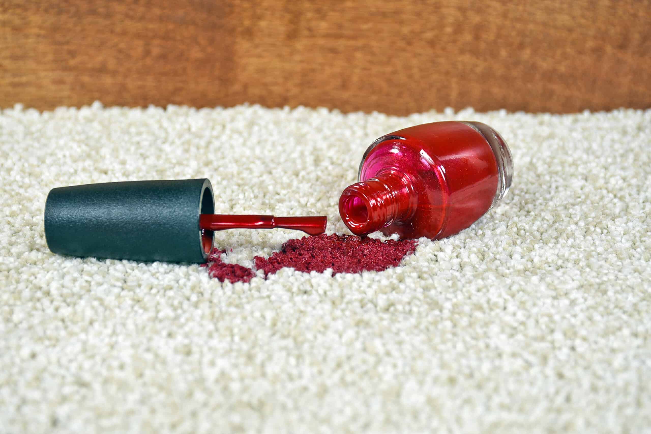 A bottle of red nail polish spilt on white carpet. There is a big stain.