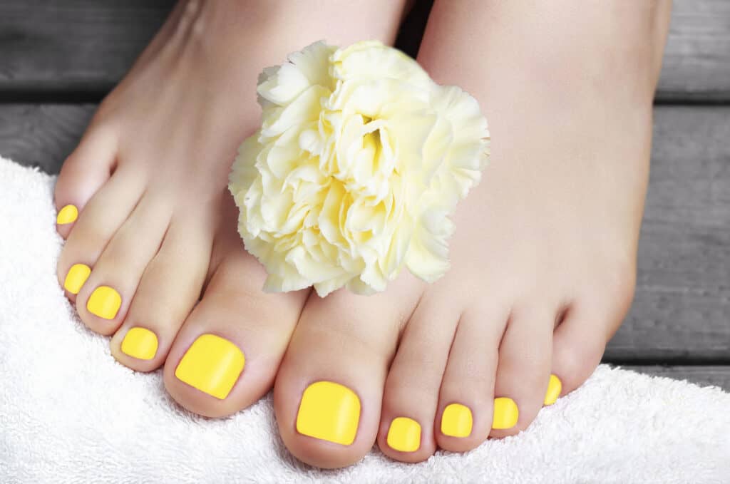 women's feel with yellow painted toenails and a white flower between her feet.