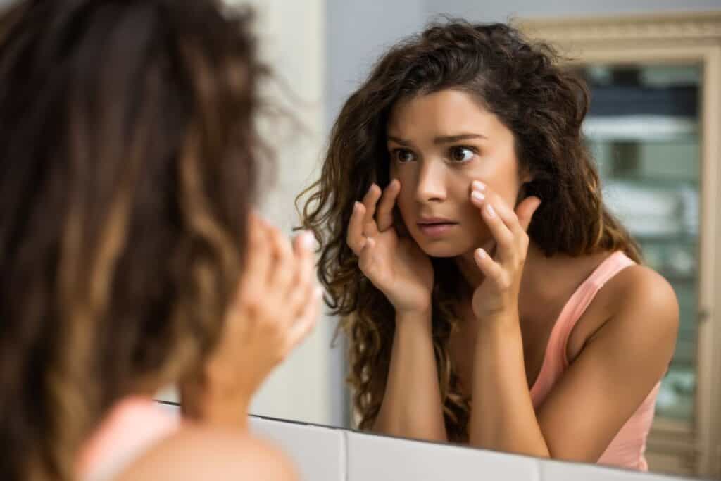 woman staring at her eyes in the mirror