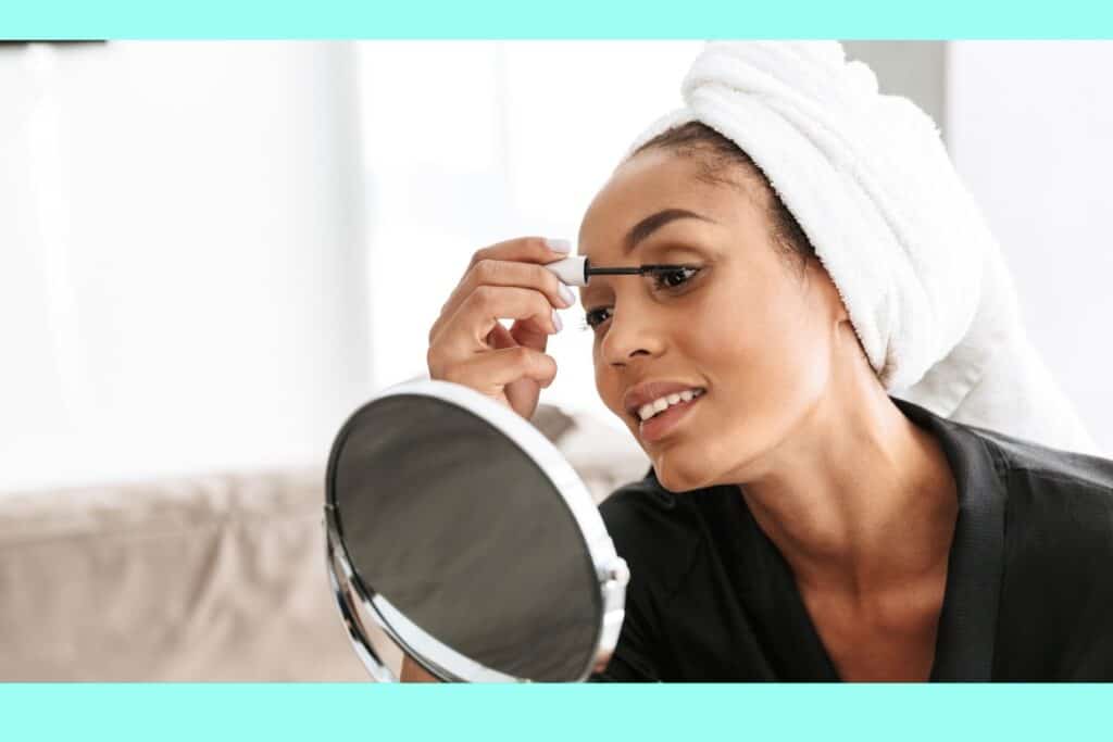 woman applying mascara on her eye while looking into the mirror